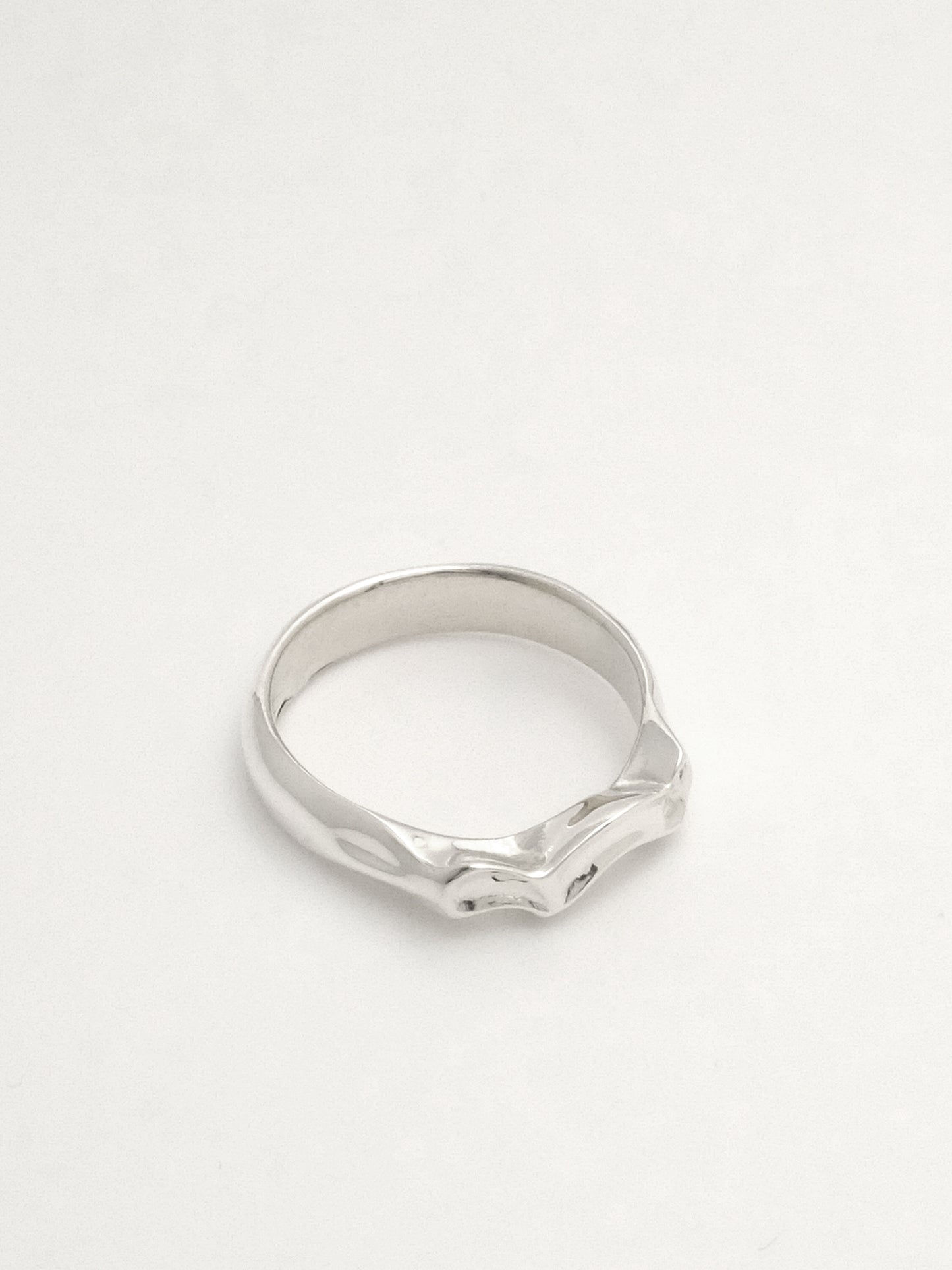 Close-up of a sterling silver ring lying on its side showing the undercut of the undulating form at the top of the band.
