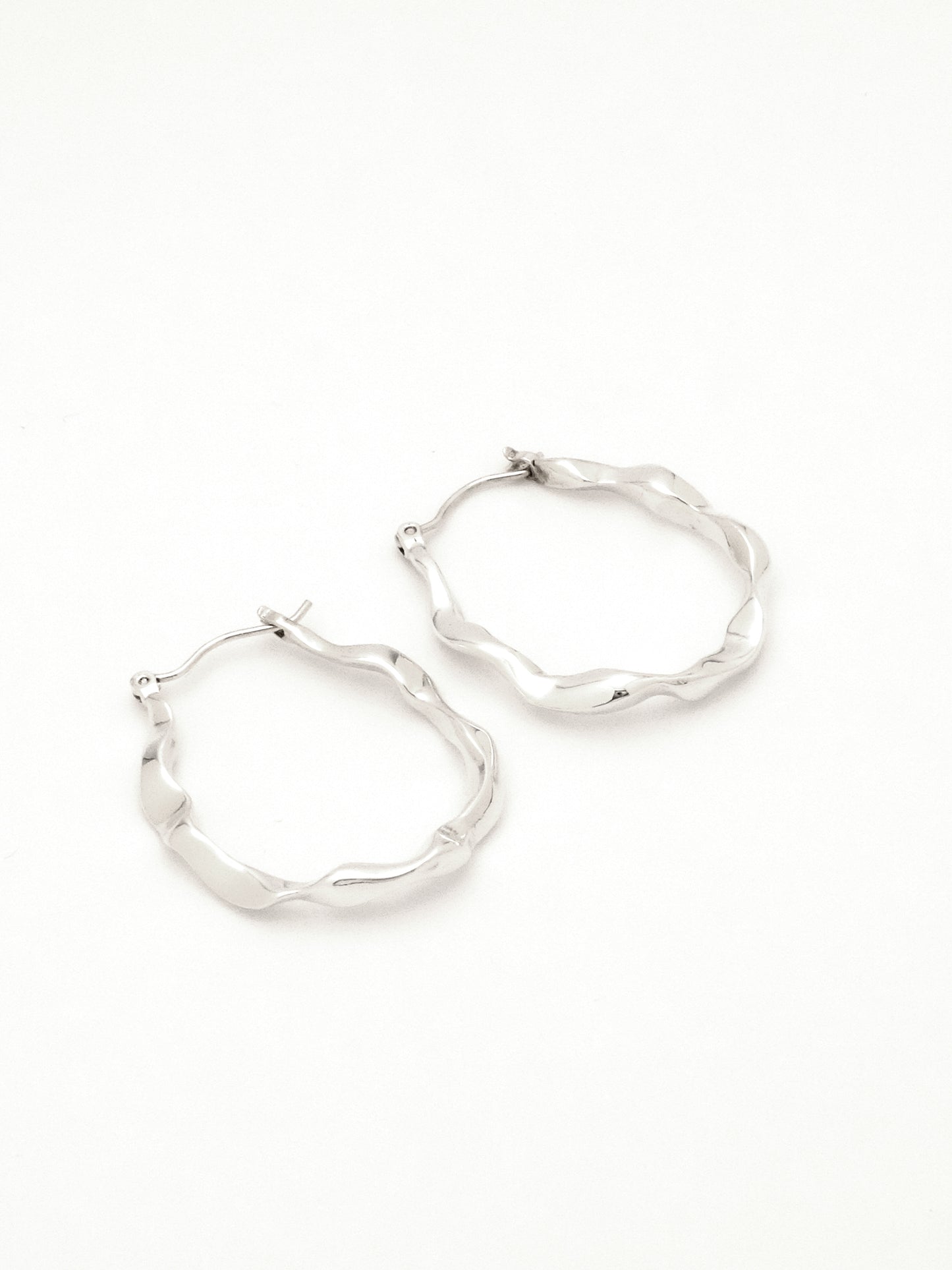 2 sterling silver hoop earrings lying on their side to show the subtle difference in each organic form, mimicking rivulets of water.