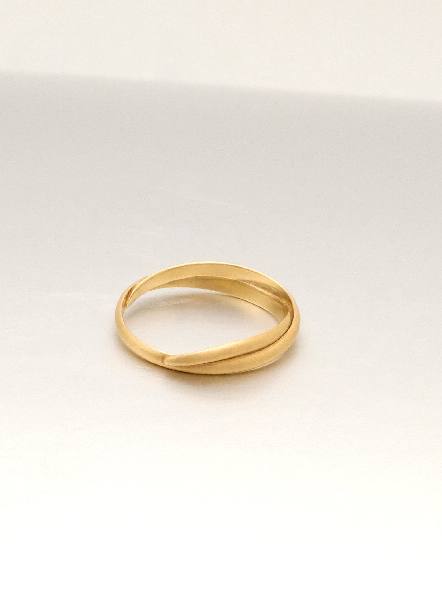 The same brushed yellow gold ring band as the previous images shown lying flat and from an angle showing the interior of the band. The wire strands layer and intersect and the tapered strand tucks back onto itself. 