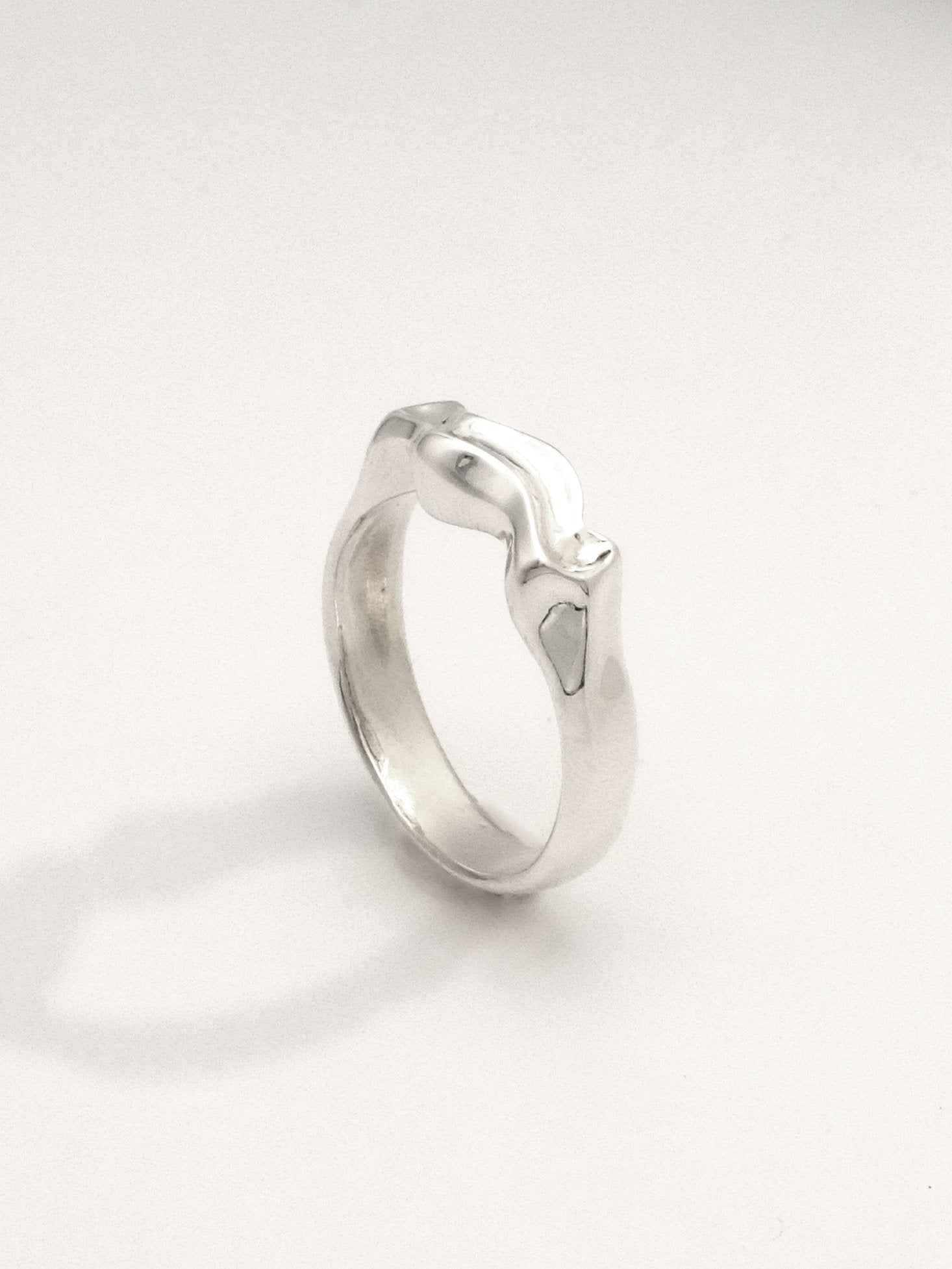 Close-up of a sterling silver ring in an upright position featuring a liquid-like form with a mirror shine finish. The ring is 5mm wide at its widest point."