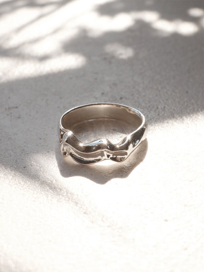 Close-up of a sterling silver ring lying in a sunbeam, with light reflecting off of the form's high points highlighting its rippling form and shining finish. The ring is 5mm wide at its widest point."