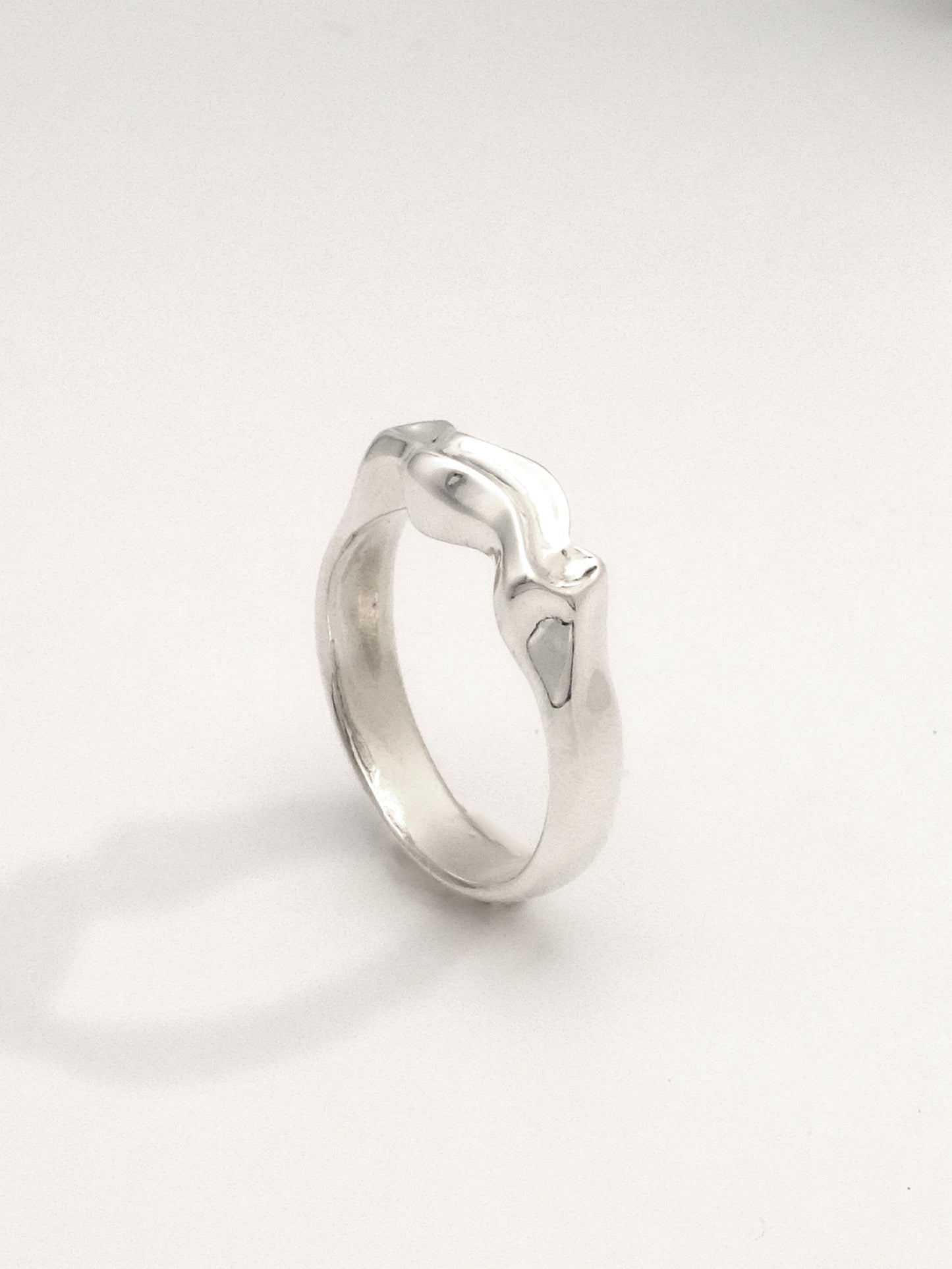 Close-up of a sterling silver ring in an upright position featuring a liquid-like form with a mirror shine finish. The ring is 5mm wide at its widest point."