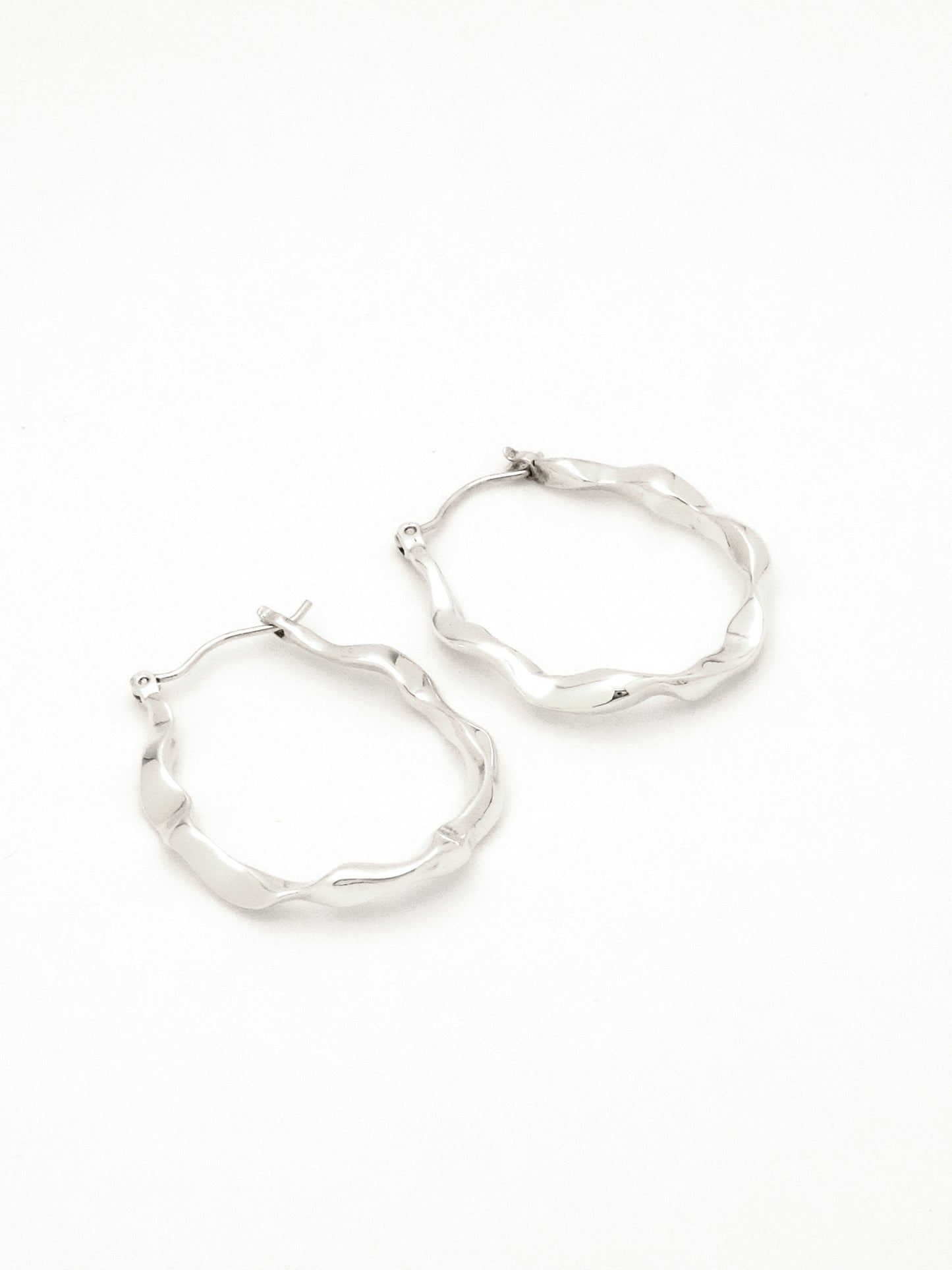 2 sterling silver hoop earrings lying on their side to show the subtle difference in each organic form, mimicking rivulets of water. 