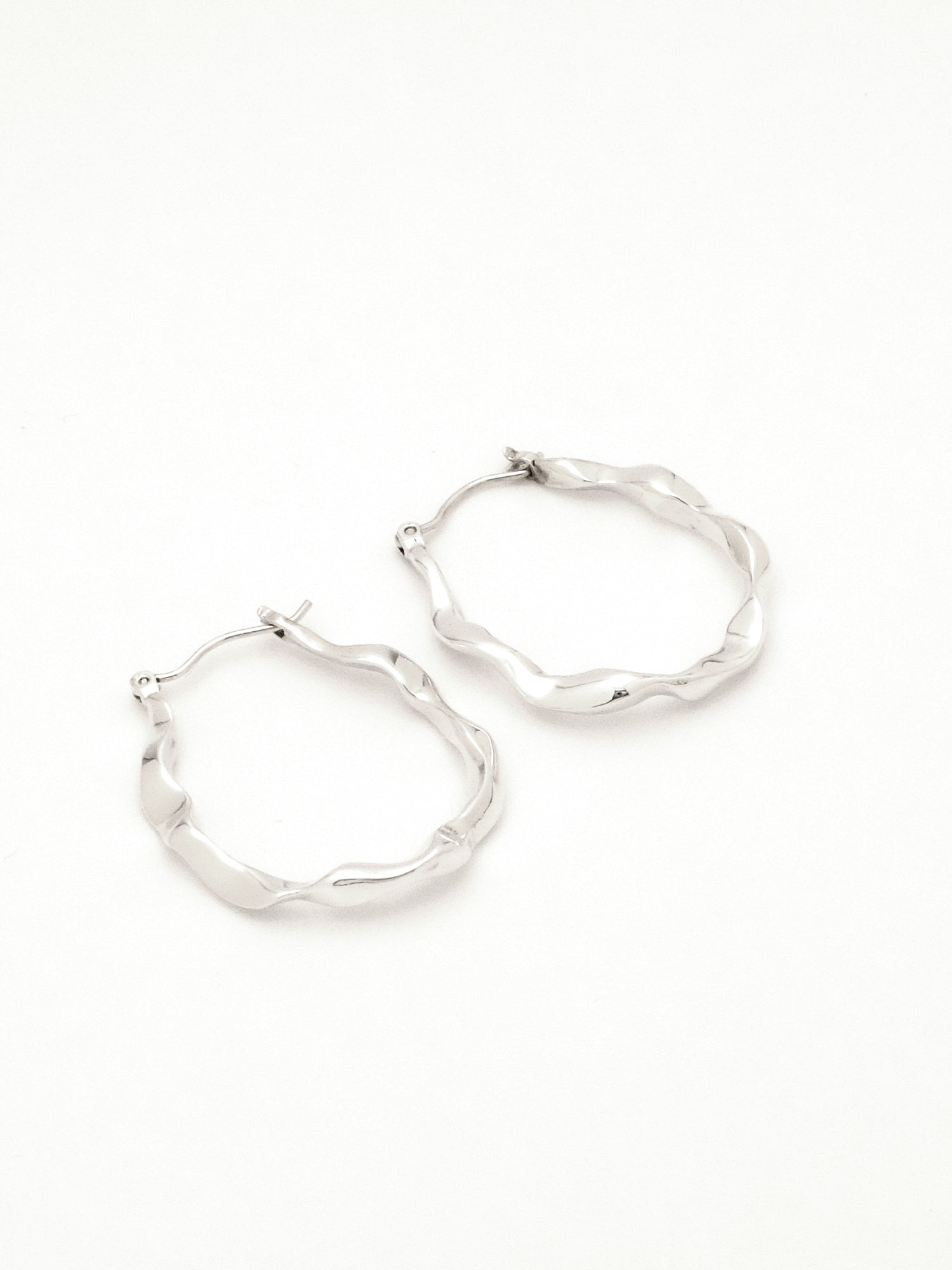 2 sterling silver hoop earrings lying on their side to show the subtle difference in each organic form, mimicking rivulets of water. 