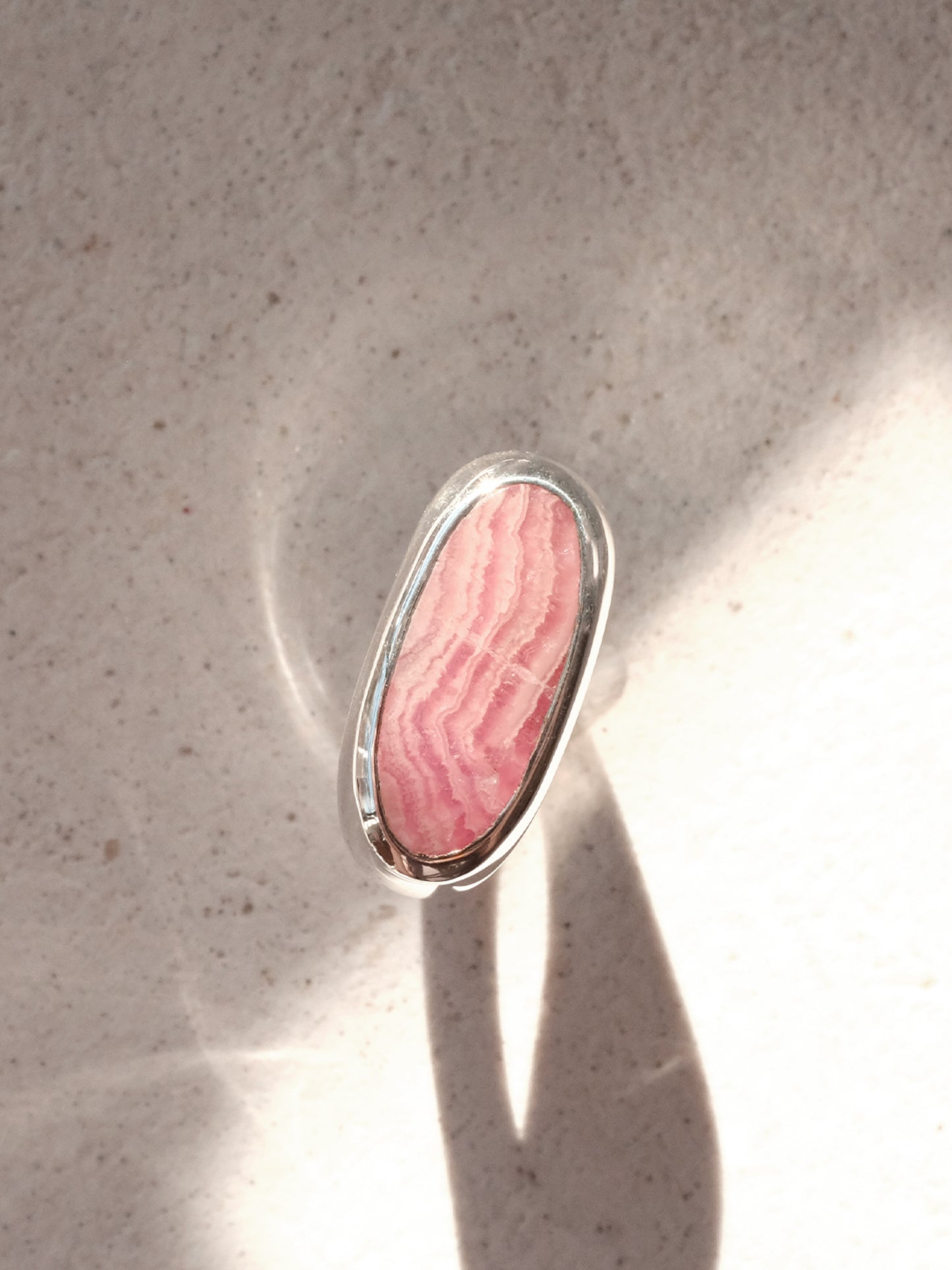 The same sterling silver signet ring with pink hued stone from the previous image, shown in a top down view in a beam of sunlight showcasing the clean and flush bezel setting, and the gradients in the stone. 