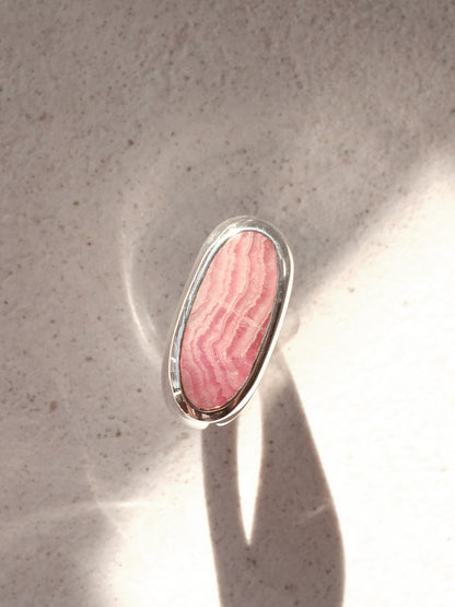 The same sterling silver signet ring with pink hued stone from the previous image, shown in a top down view in a beam of sunlight showcasing the clean and flush bezel setting, and the gradients in the stone. 