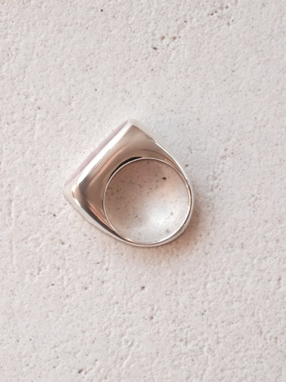 The same sterling silver signet ring with stone from the previous images shown in top-down of the ring's complete form lying flat, to show it's uniform shape and mirror finish.