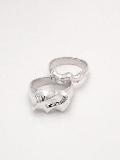 Two sterling silver rings displayed as a pair, showcasing one wide and one narrow band. Both rings feature an undulating, water-like form with a mirror shine finish.