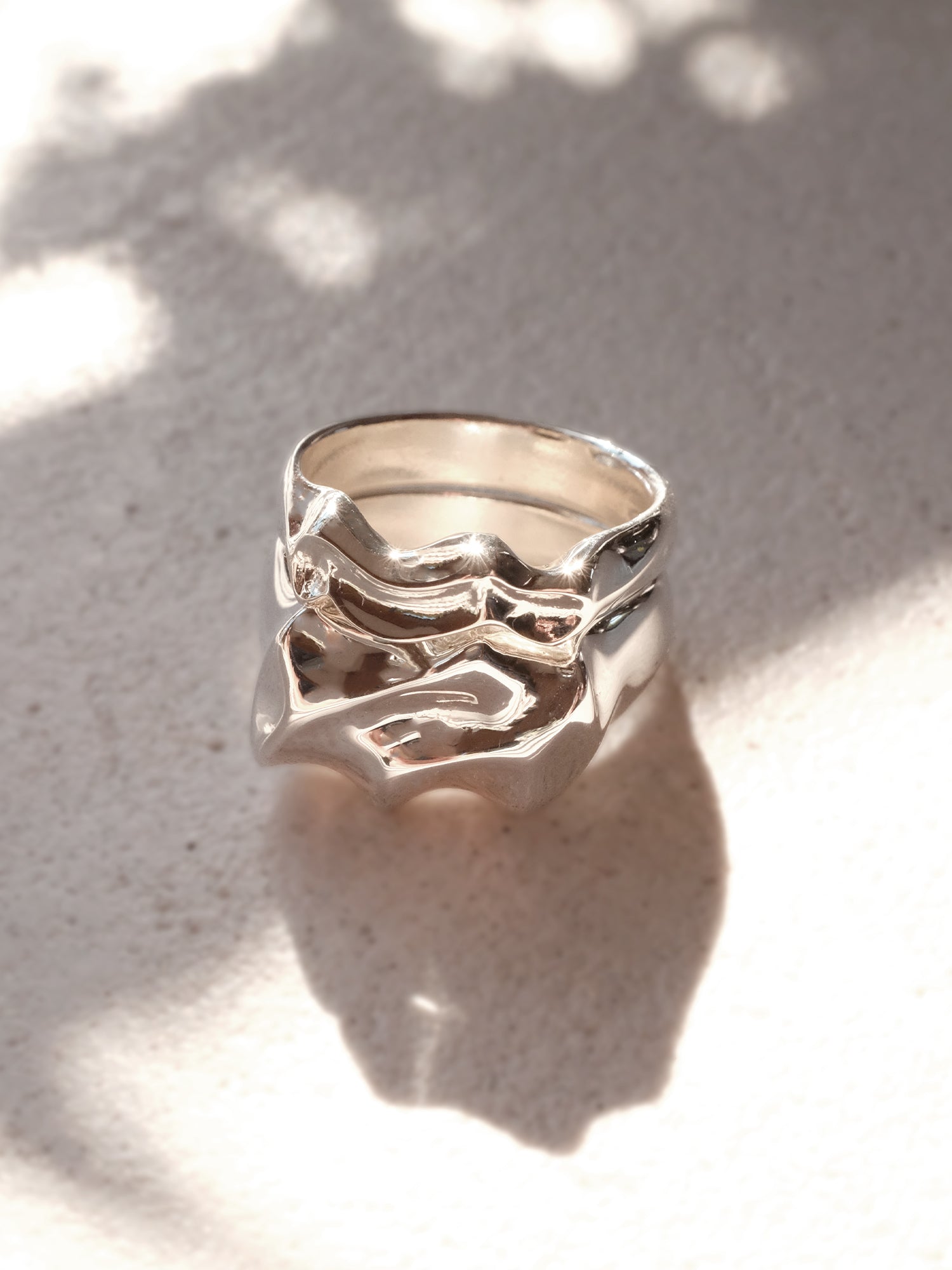 Two sterling silver rings displayed as a stacked pair, showcasing how the water-like forms tesselate together. The light and shadow on the rings highlight how the metal illuminates like the surface of water.