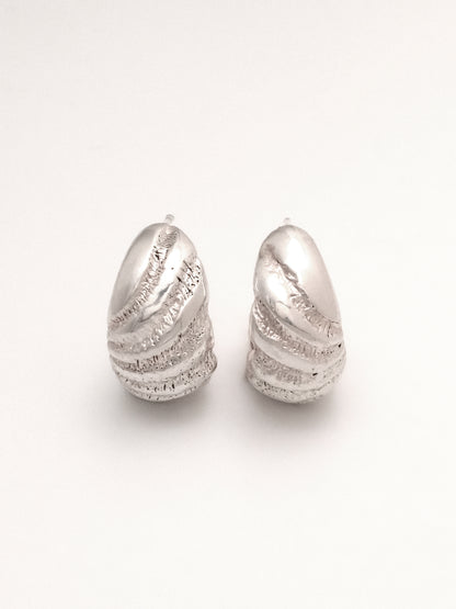 A close up of the same pair of Sterling Silver hoop earrings, positioned upright and side by side to show the radiating texture and subtle organic difference of the mirrored right and left. 